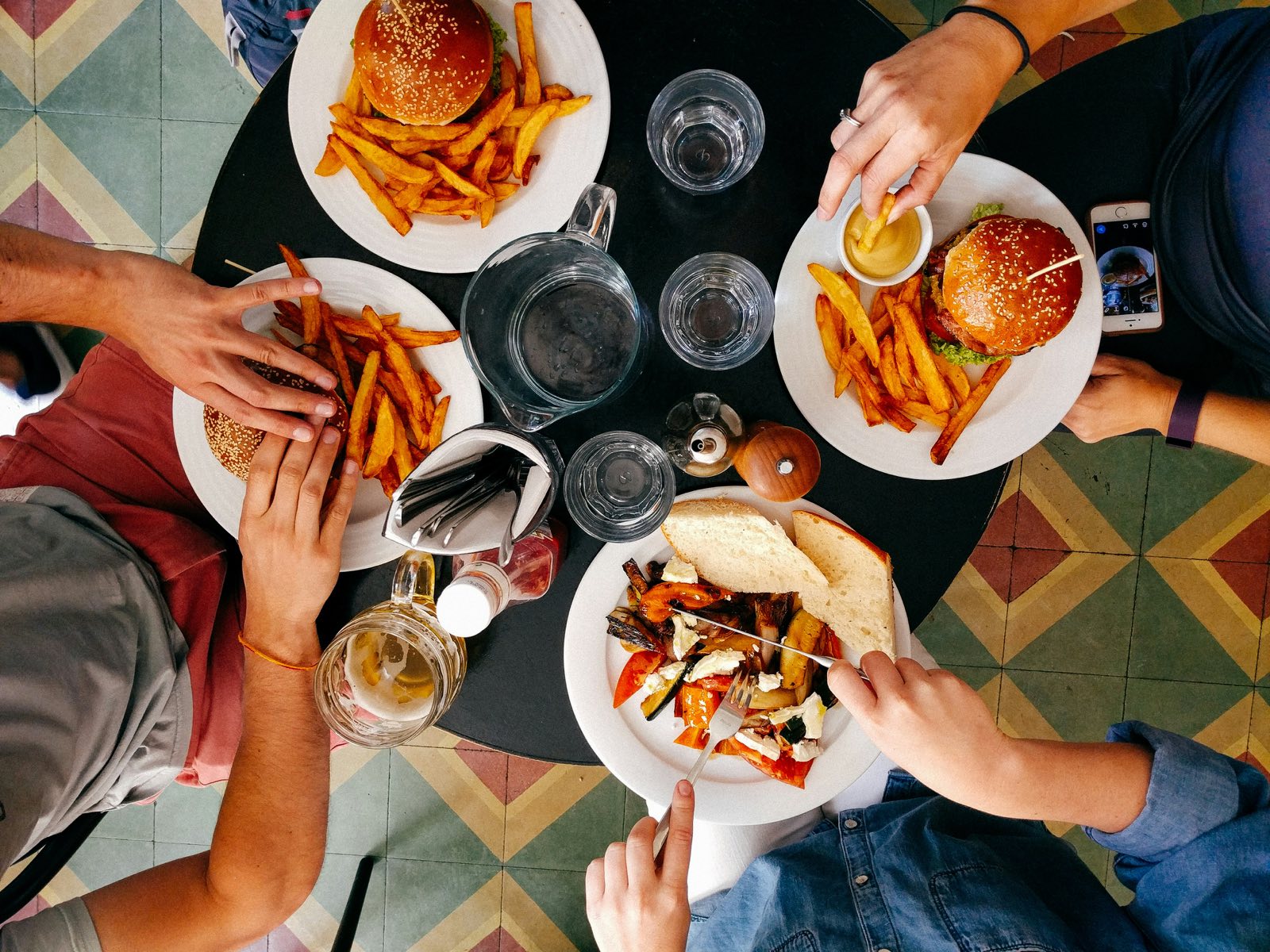 Una mesa vista desde arriba: hamburguesas, papitas fritas y las manos de la comunidad compartiendo el plato